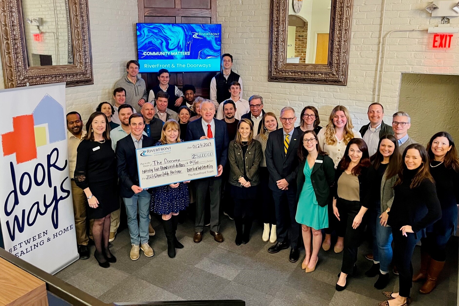 Large group holding a large check from RiverFront to The Doorways. The Doorways banner is also visible as is a screen recognizing the partnership..