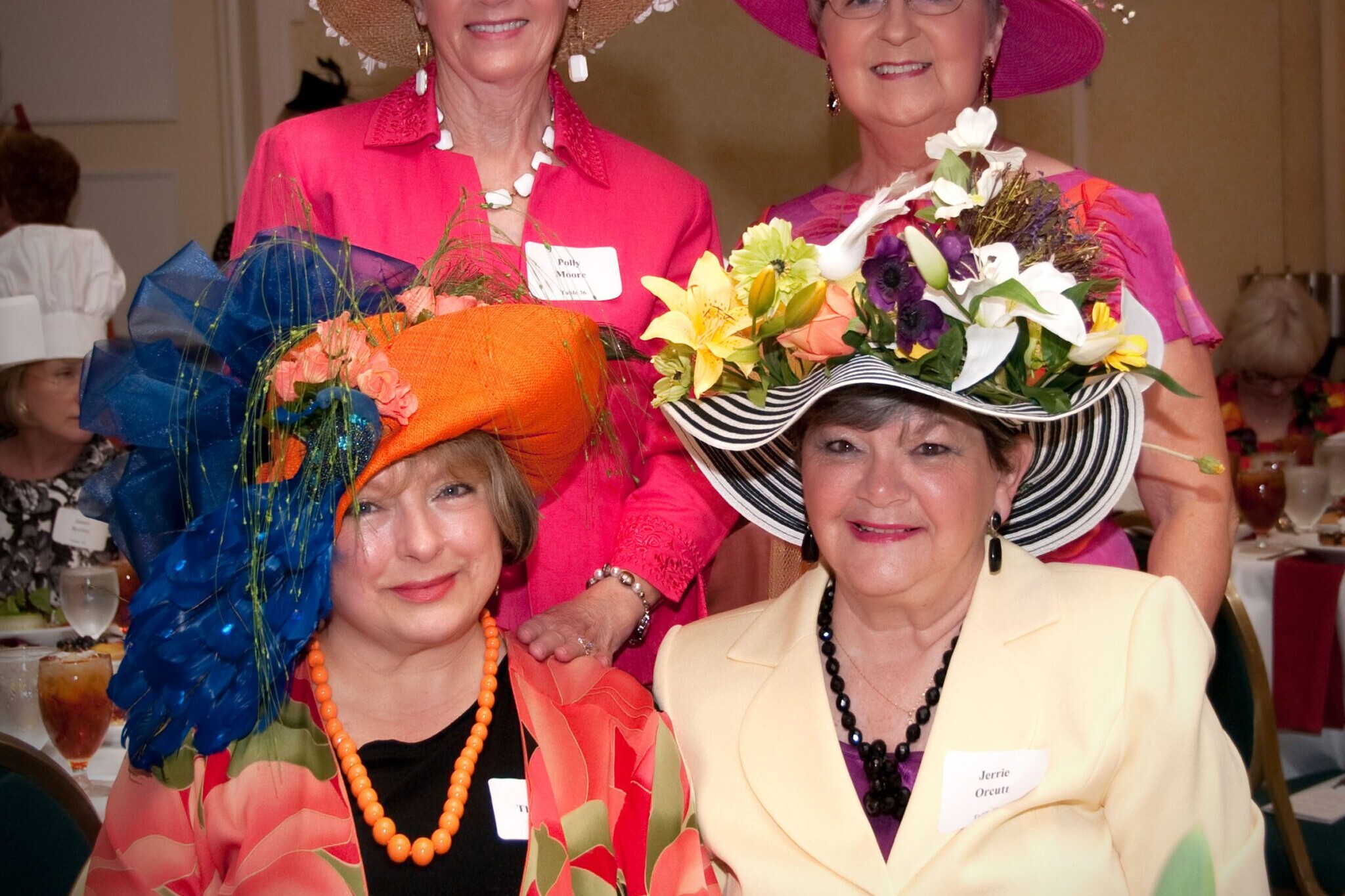 Four smiling individuals wear elaborate hats