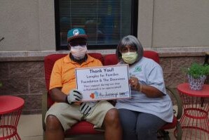 Two smiling adults hold a thank you sign in the garden of The Doorways