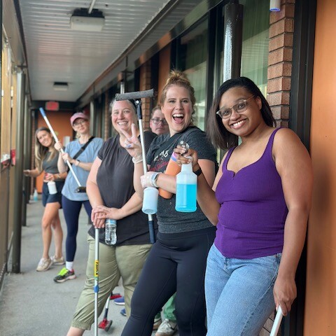 A group of 6 smiling individuals pose with squeegees and windex bottles