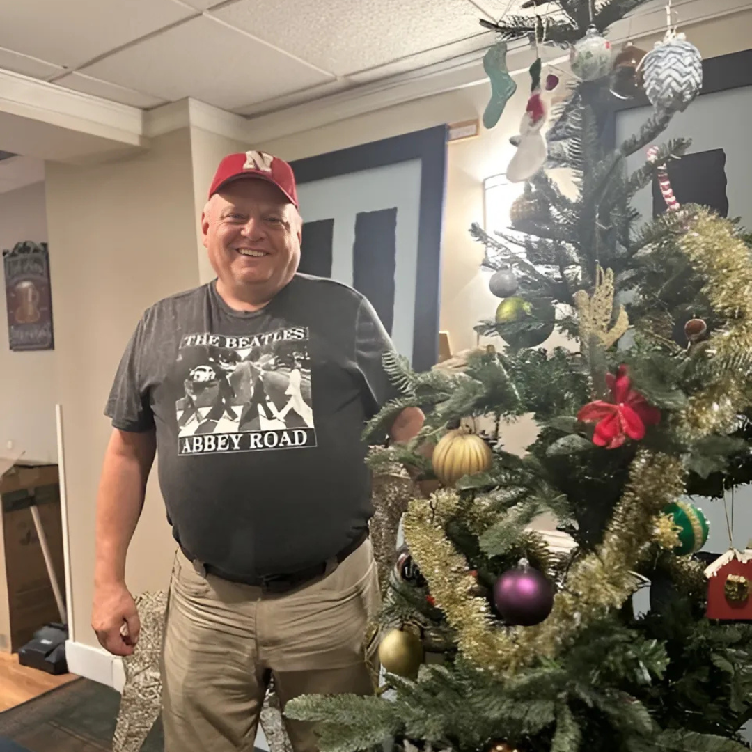 A smiling adult stands beside a decorated Christmas tree in the dining room of The Doorways