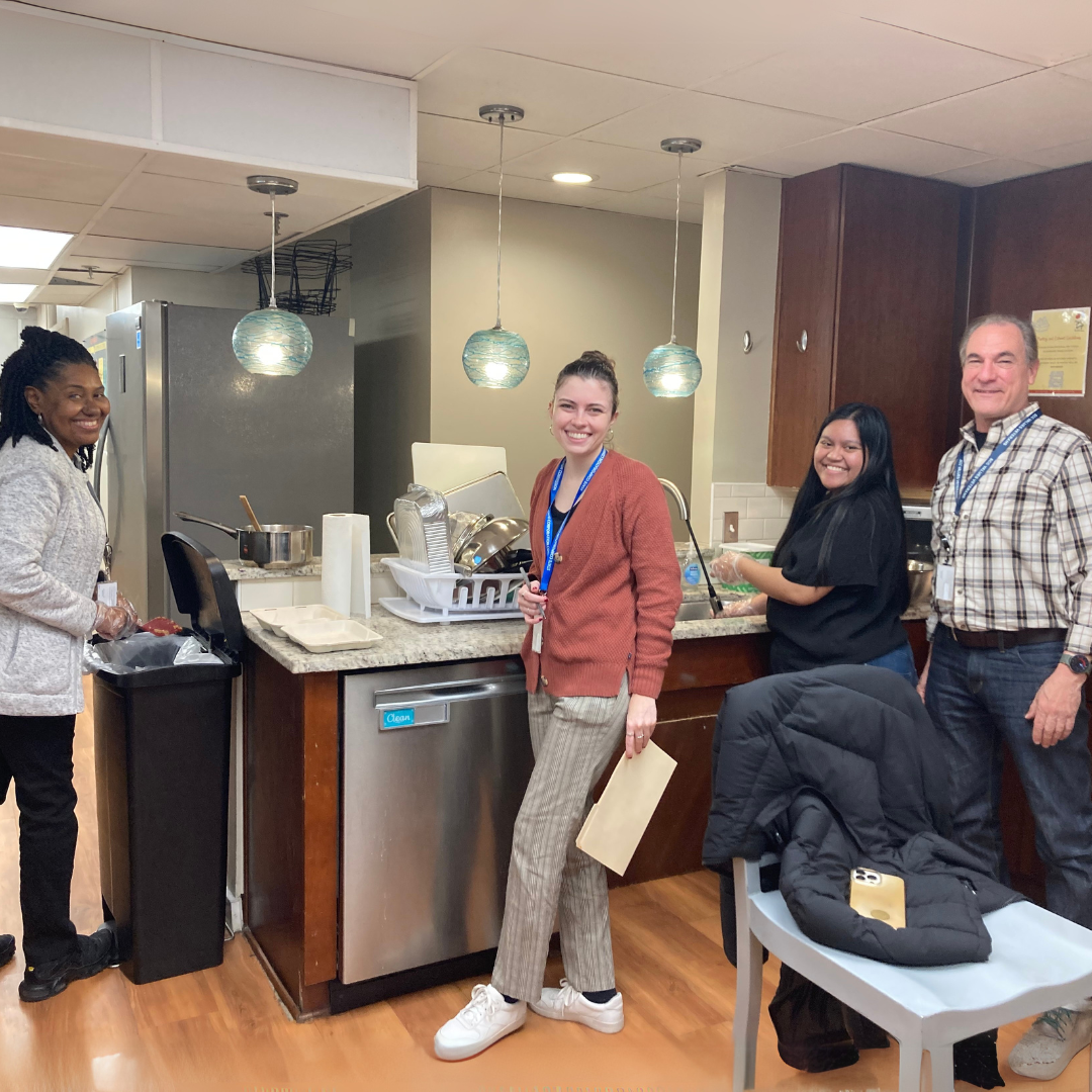 Four smiling adults prepare meals in the main kitchen of The Doorways