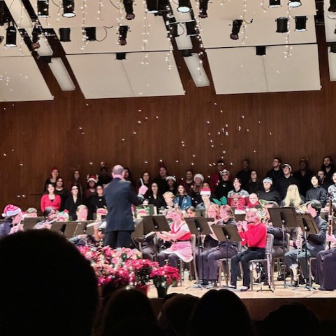 A group of V-C-U students play instruments and sing as a conductor leads them while fake snow falls