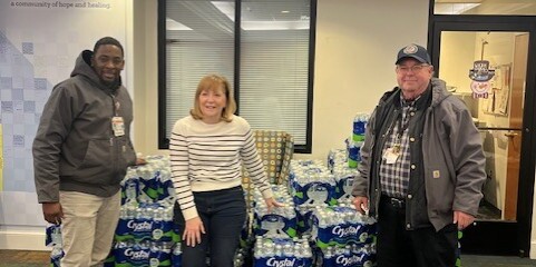 VCU Health water delivery team with three smiling individuals and a massive pile of water behind them