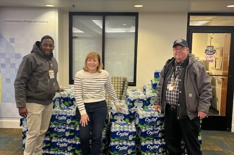 VCU Health water delivery team with three smiling individuals and a massive pile of water behind them