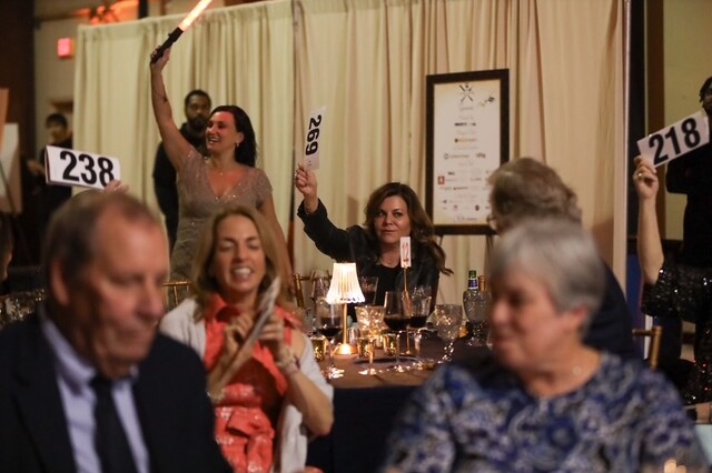 smiling adults hold up paddles during a live auction